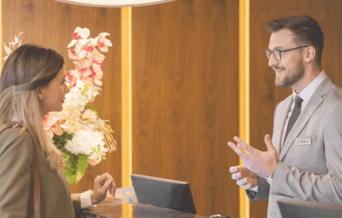 Hotel receptionist assisting a guest at the front desk, representing hospitality and guest experience.