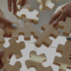 Group of people connecting large wooden puzzle pieces – teamwork, collaboration, and HR strategy at BARE International.