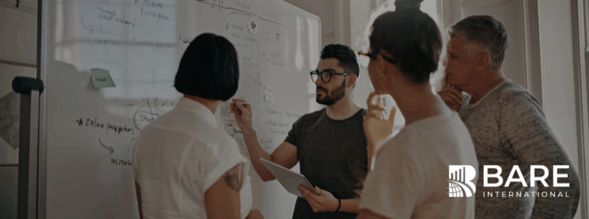 Team in a meeting discussing strategies at a whiteboard – leadership, planning, and innovation at BARE International.