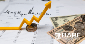 Yellow upward financial arrow on top of stacked coins with cash and performance charts, symbolizing revenue protection and the impact of mystery shopping on preventing CX-related profit leaks.